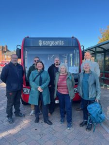 Group of 7 people in front of a red single decker bus.