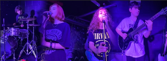 Teenage music band, two girls are singing, 1 boy playing on guitar and another one on drums<br />
