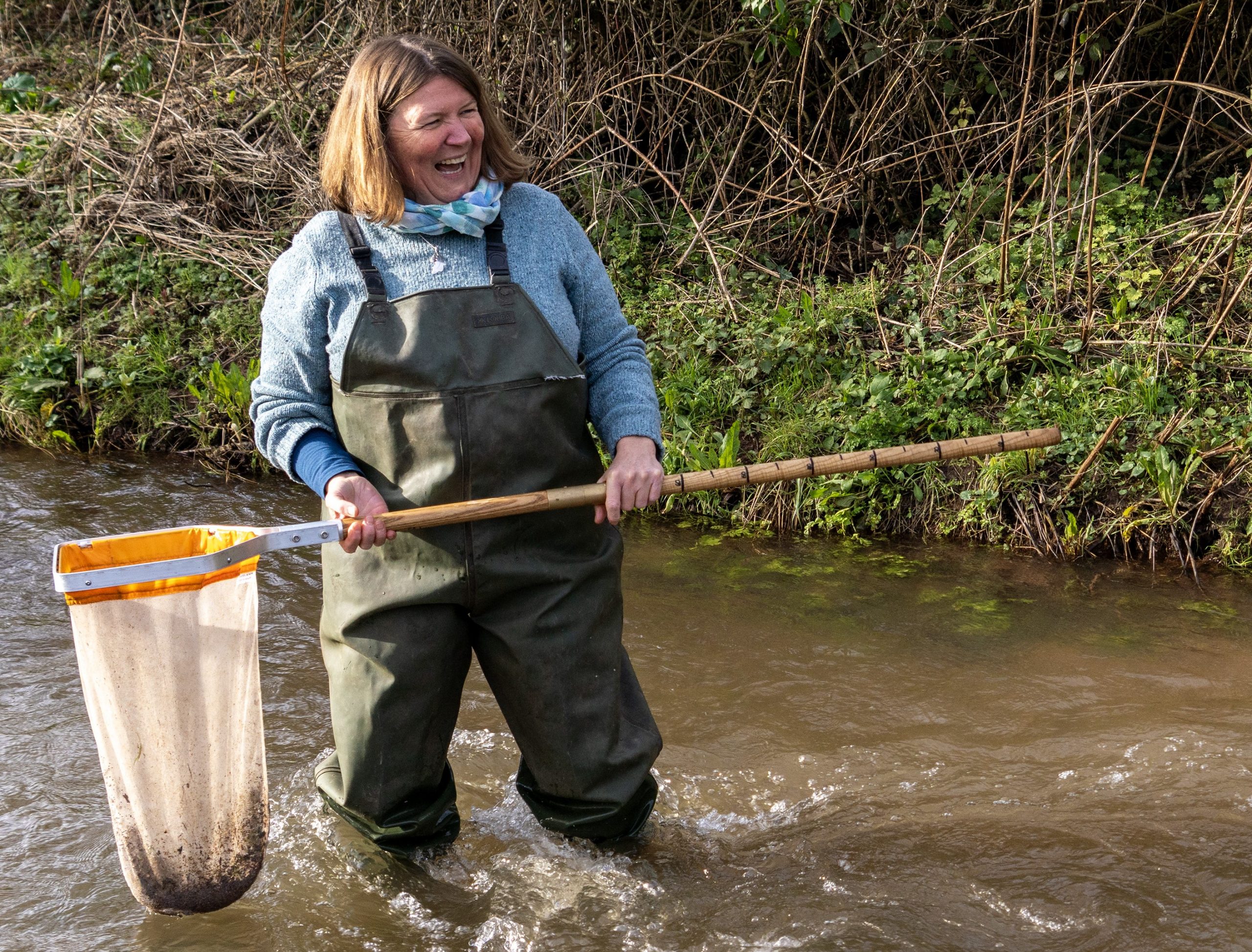 Ellie is standing in the river and holding the net with ground