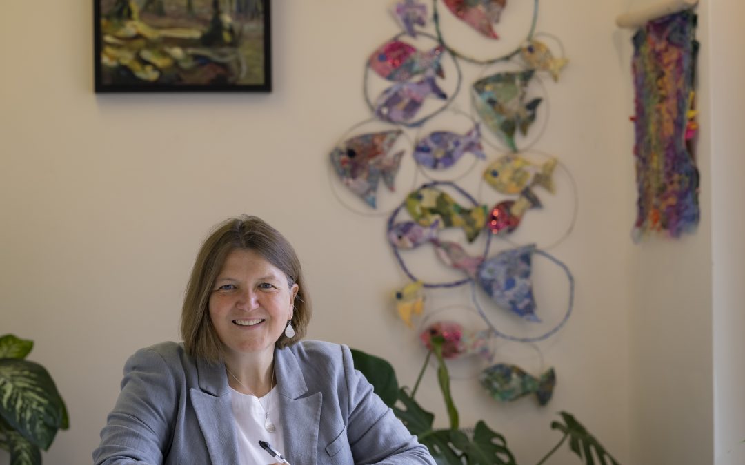 Ellie Chowns sitting at her desk with colourful wall hangings behind her.
